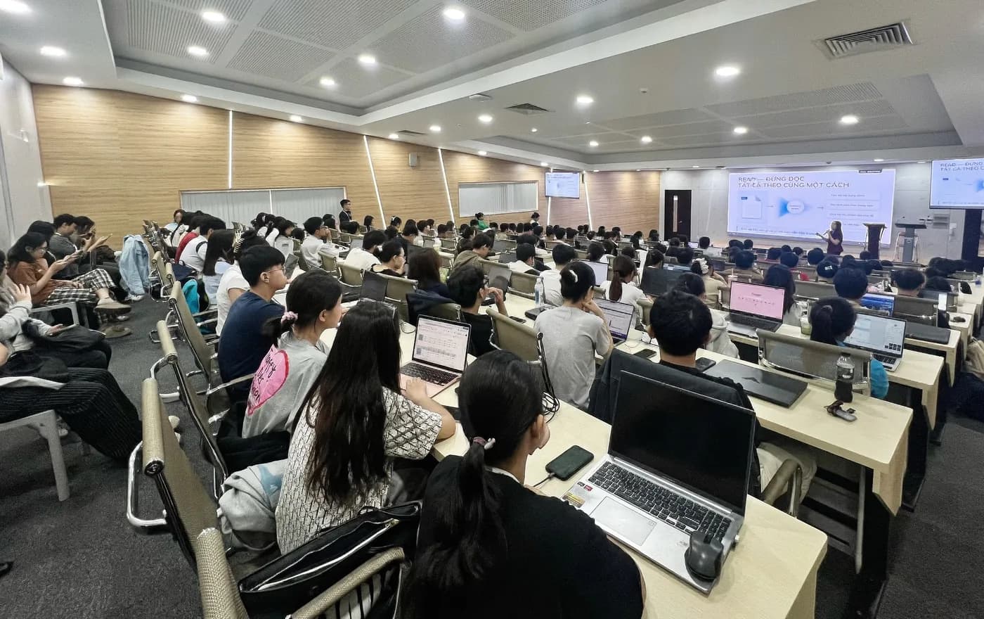 Toàn cảnh hội trường kín chỗ, sinh viên ngồi theo dãy bàn với laptop mở sẵn