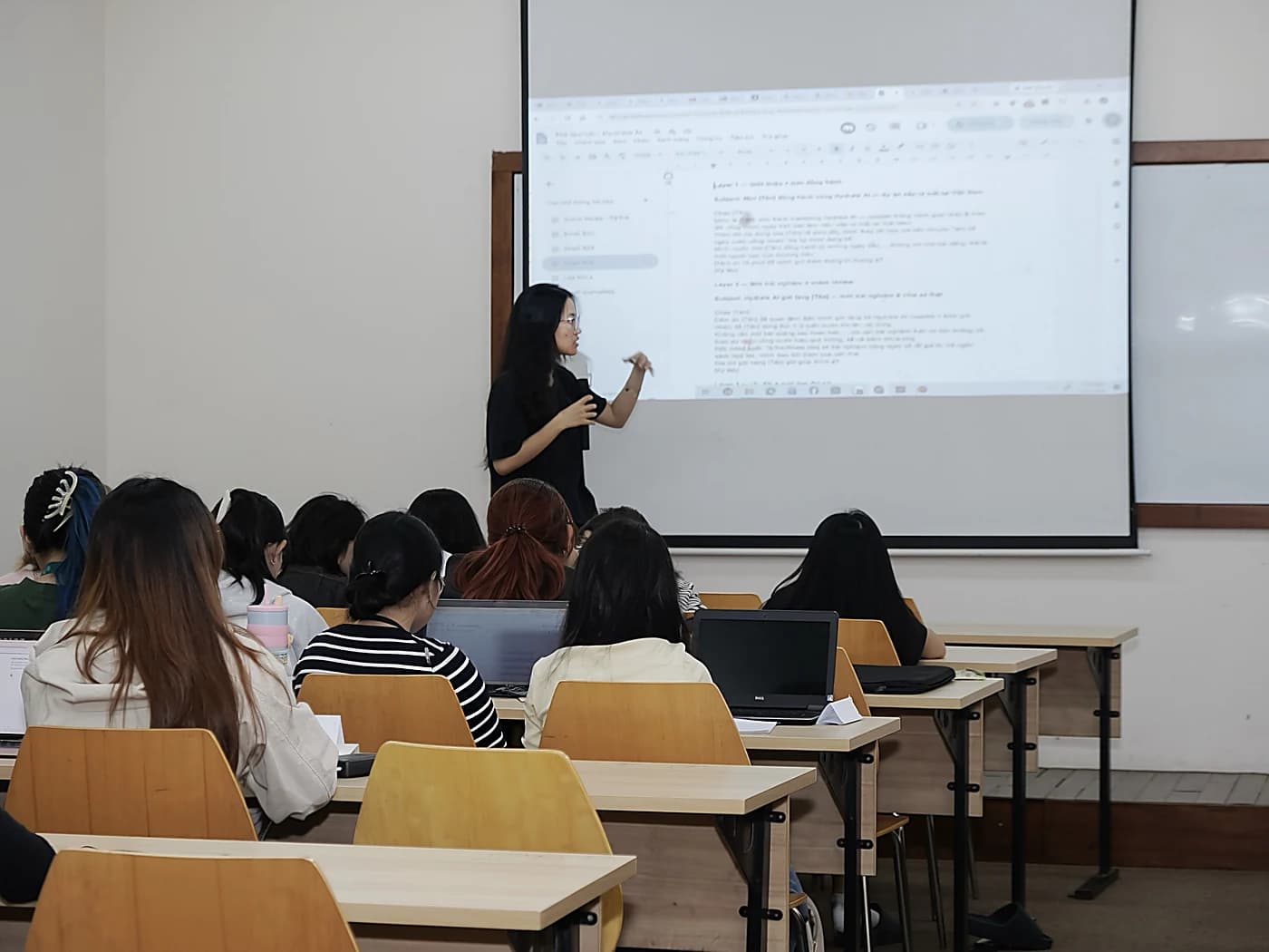 Một sinh viên đứng trình bày bài làm nhóm trước màn chiếu
