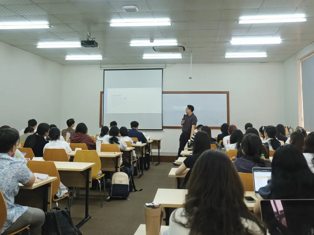 Lớp học nhìn từ cuối phòng, sinh viên hướng về màn chiếu